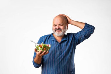 60 'lı yaşlarda emekli Hintli yaşlı adam sağlıklı yeşil sebze salatası yiyor.