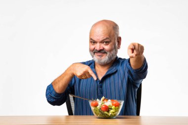 60 'lı yaşlarda emekli Hintli yaşlı adam sağlıklı yeşil sebze salatası yiyor.