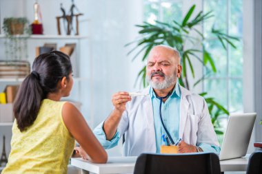 Indian asian senior elderly matured male doctor with Girl child patient in clinic clipart