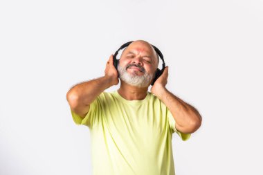 Hint asıllı emekli yaşlı adam müzik dinliyor, dans ediyor, kulaklık takıyor, beyaz arka planda izole edilmiş..