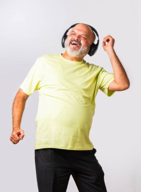 Hint asıllı emekli yaşlı adam müzik dinliyor, dans ediyor, kulaklık takıyor, beyaz arka planda izole edilmiş..
