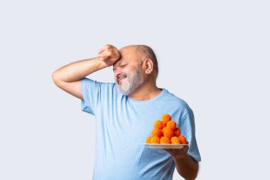 Yaşlı yaşlı Hintli adam beyaz arka planda tatlı boondi laddu ya da laddu yiyor ya da tutuyor.
