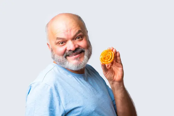 Stock image Indin asian senior elderly man eats spiral Jalebi or Jilebi against white background