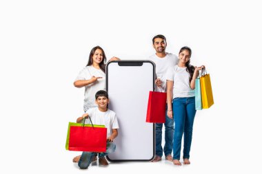 Hintli Asyalı bir aile ellerinde alışveriş torbalarıyla uzun bir telefonun yanında duruyor ve teklif sunuyor ya da sunuyor.