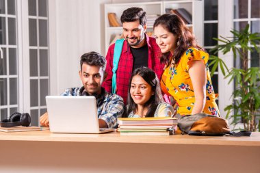 Hintli dört üniversite öğrencisi ya da üniversite öğrencileri masada çalışmak için dizüstü bilgisayar kullanıyor