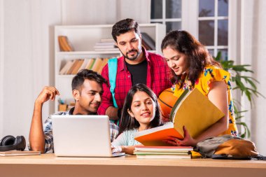 Hintli dört üniversite öğrencisi ya da üniversite öğrencileri masada çalışmak için dizüstü bilgisayar kullanıyor