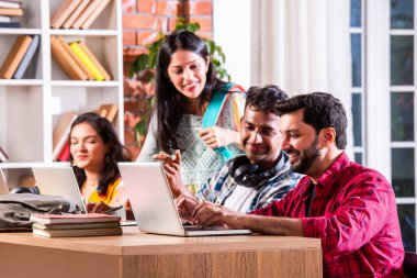 Hintli dört üniversite öğrencisi ya da üniversite öğrencileri masada çalışmak için dizüstü bilgisayar kullanıyor