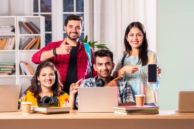 Hintli dört üniversite öğrencisi ya da üniversite öğrencileri masada çalışmak için dizüstü bilgisayar kullanıyor