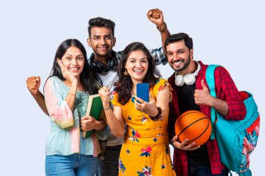 Bir grup Hintli Asyalı üniversite öğrencisi beyaz arka plana karşı selfie ya da video izlemek için akıllı telefon kullanıyor.