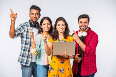 Hintli Asyalı üniversite öğrencileri dizüstü bilgisayarlarını kullanarak boş yerleri gösteriyorlar veya başarıyı kutluyorlar.