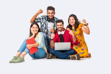 Hintli Asyalı üniversite öğrencileri dizüstü bilgisayarlarını kullanarak boş yerleri gösteriyorlar veya başarıyı kutluyorlar.