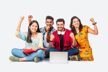 Hintli Asyalı üniversite öğrencileri dizüstü bilgisayarlarını kullanarak boş yerleri gösteriyorlar veya başarıyı kutluyorlar.