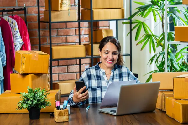 Stock image Indian asian Woman Managing Online Orders with Laptop and Smartphone, Ready to Ship from Warehouse