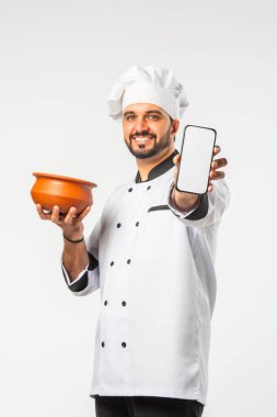 Beyaz elbiseli Hintli şef elinde akıllı telefon ve biryani terracotta otu tutuyor..