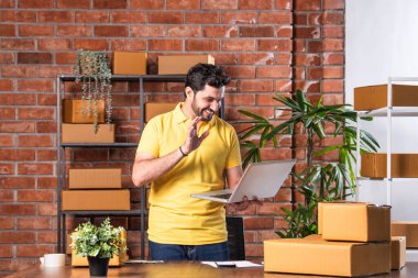 Hintli Asyalı Adam Dizüstü bilgisayarlı ve akıllı telefonlu online siparişleri yönetiyor, Depo 'dan gönderilmeye hazır.