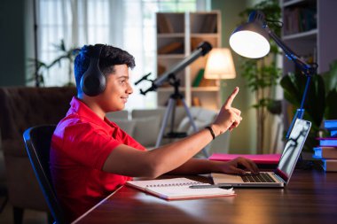 Bilgisayar, kulaklık, internet dersi için akıllı telefon ve ödev kullanan Hintli Asyalı genç çocuk.