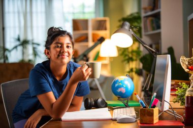 Hintli Asyalı kız evde ders çalışıyor ve bardakta süt enerjisi içiyor.