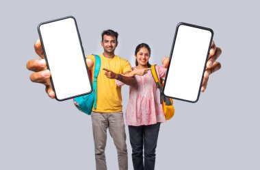 Hintli genç üniversite öğrencileri ellerinde büyük akıllı telefonlar boş ekran gösteriyor.