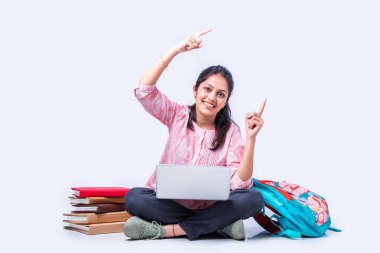 Hintli Asyalı üniversite öğrencisi dizüstü bilgisayarla beyaz arka planda otururken okuyor.