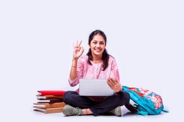 Hintli Asyalı üniversite öğrencisi dizüstü bilgisayarla beyaz arka planda otururken okuyor.