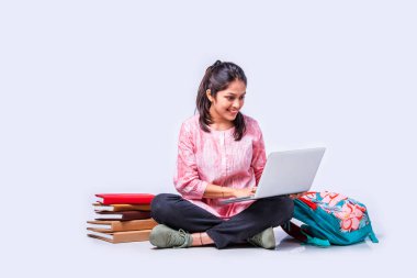 Hintli Asyalı üniversite öğrencisi dizüstü bilgisayarla beyaz arka planda otururken okuyor.