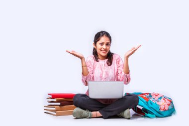 Hintli Asyalı üniversite öğrencisi dizüstü bilgisayarla beyaz arka planda otururken okuyor.