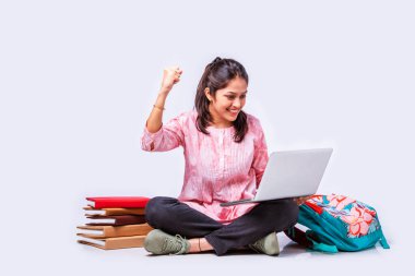 Hintli Asyalı üniversite öğrencisi dizüstü bilgisayarla beyaz arka planda otururken okuyor.