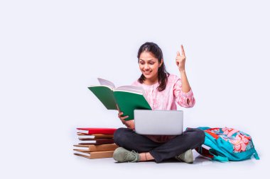 Hintli Asyalı üniversite öğrencisi dizüstü bilgisayarla beyaz arka planda otururken okuyor.