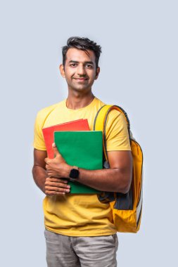 Kitaplar, dizüstü bilgisayarlar ve sırt çantasıyla beyazlara karşı duran mutlu Hintli üniversiteli çocuk.