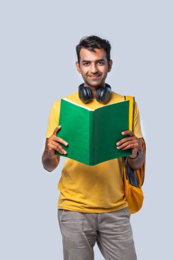 Kitaplar, dizüstü bilgisayarlar ve sırt çantasıyla beyazlara karşı duran mutlu Hintli üniversiteli çocuk.