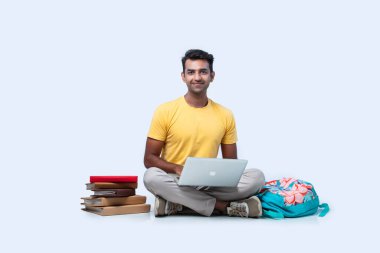 Hintli erkek üniversite öğrencisi beyaz arka planda tek başına otururken okuyor.