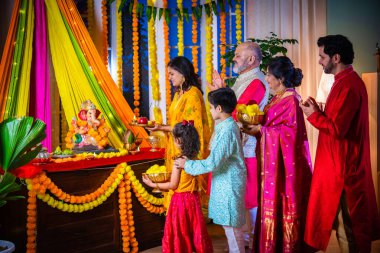 Indian family in traditional wear performing Ganesh Puja or Aarti at home, a religious ritual clipart