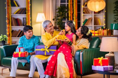 Aile Diwali gecesini kutluyor, ladaları paylaşıyor ve hediyelerle dolu bir kanepede neşe saçıyor.