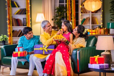 Aile Diwali gecesini kutluyor, ladaları paylaşıyor ve hediyelerle dolu bir kanepede neşe saçıyor.