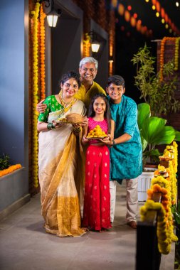 Çocuklu mutlu Hintli aile balkonda Diwali 'yi kutluyor, ellerinde Pooja thali, besan laddu