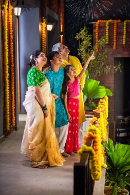 Küçük bir kızken heyecanlı bir şekilde gökyüzünü işaret eden Diwali havai fişeklerini izleyen Hint ailesi.