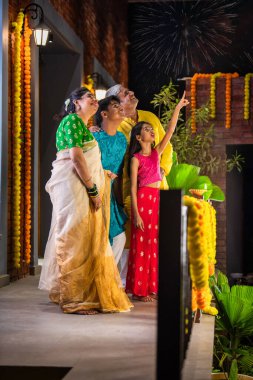 Küçük bir kızken heyecanlı bir şekilde gökyüzünü işaret eden Diwali havai fişeklerini izleyen Hint ailesi.