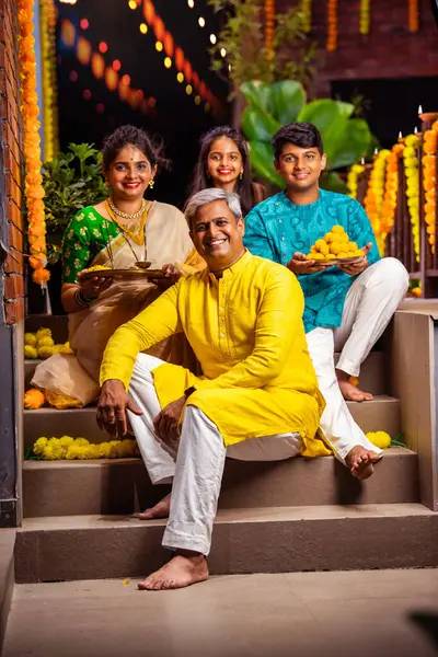 Stock image Indian family of four celebrating Diwali on stairs, holding festive items, smiling at the camera