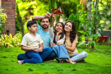 Çocukları parkta oturmuş birbirlerini kucaklayan mutlu Hintli çift ve kızlarının kucağına aldığı oyuncak uçağa hayranlık duyuyorlar. Aşkı, aile zamanını, hayal gücünü ve beraberliği sembolize ediyorlar.