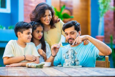 Hintli genç baba Ganesh Chaturthi için çevre dostu Ganesh putu yapıyor ve çocuklara nasıl yapılacağını öğretiyor. Güzel karısı hayranlıkla bakıyor. Aile bahçede oturuyor.