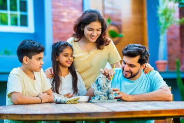 Hintli genç baba Ganesh Chaturthi için çevre dostu Ganesh putu yapıyor ve çocuklara nasıl yapılacağını öğretiyor. Güzel karısı hayranlıkla bakıyor. Aile bahçede oturuyor.