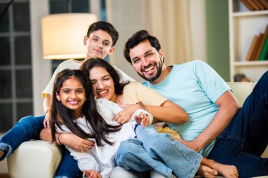 Dört kişilik neşeli Hintli aile evde kaliteli zaman geçiriyorlar. Aileler ve çocuklar kanepede oturuyor, birlikte gülüyor ve oynuyorlar. Mutlu aile bağları ve aşk anları yakalıyorlar.