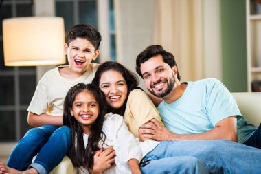 Dört kişilik neşeli Hintli aile evde kaliteli zaman geçiriyorlar. Aileler ve çocuklar kanepede oturuyor, birlikte gülüyor ve oynuyorlar. Mutlu aile bağları ve aşk anları yakalıyorlar.