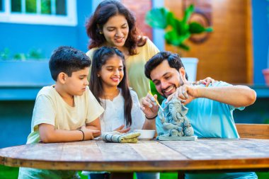 Hintli genç baba Ganesh Chaturthi için çevre dostu Ganesh putu yapıyor ve çocuklara nasıl yapılacağını öğretiyor. Güzel karısı hayranlıkla bakıyor. Aile bahçede oturuyor.