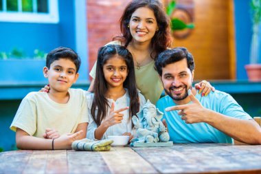 Hintli genç baba Ganesh Chaturthi için çevre dostu Ganesh putu yapıyor ve çocuklara nasıl yapılacağını öğretiyor. Güzel karısı hayranlıkla bakıyor. Aile bahçede oturuyor.