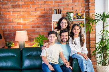 Dört kişilik neşeli Hintli aile evde kaliteli zaman geçiriyorlar. Aileler ve çocuklar kanepede oturuyor, birlikte gülüyor ve oynuyorlar. Mutlu aile bağları ve aşk anları yakalıyorlar.