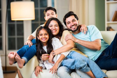 Dört kişilik neşeli Hintli aile evde kaliteli zaman geçiriyorlar. Aileler ve çocuklar kanepede oturuyor, birlikte gülüyor ve oynuyorlar. Mutlu aile bağları ve aşk anları yakalıyorlar.