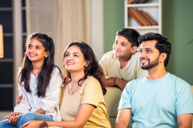 Dört kişilik neşeli Hintli aile evde kaliteli zaman geçiriyorlar. Aileler ve çocuklar kanepede oturuyor, birlikte gülüyor ve oynuyorlar. Mutlu aile bağları ve aşk anları yakalıyorlar.