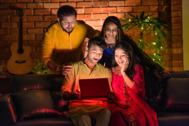 Hintli aile veya genç çiftler Diwali 'yi evde kutluyorlar, koltukta oturuyorlar, parlayan sürpriz bir hediye kutusu açıyorlar, Hindu bayramı boyunca birlikte neşe ve heyecan paylaşıyorlar.