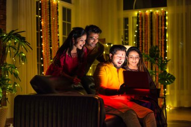 Hintli aile veya genç çiftler Diwali 'yi evde kutluyorlar, koltukta oturuyorlar, parlayan sürpriz bir hediye kutusu açıyorlar, Hindu bayramı boyunca birlikte neşe ve heyecan paylaşıyorlar.